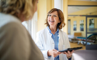 Shot of a smiling senior doctor with a digital tablet talking to a female patient at hospital. Medical professional discussing with woman at nursing home.
